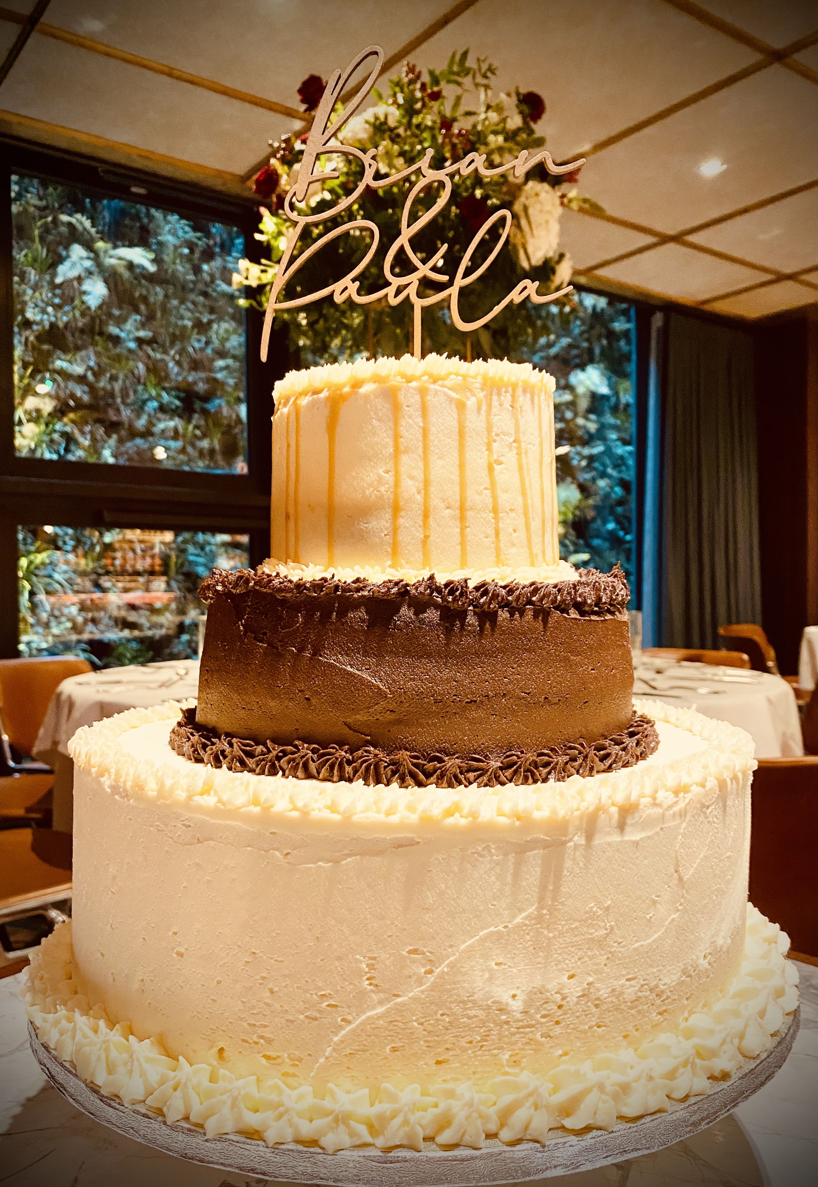 a 3 tier wedding cake with a sign on top that says "Brian & Paula" in cursive lettering